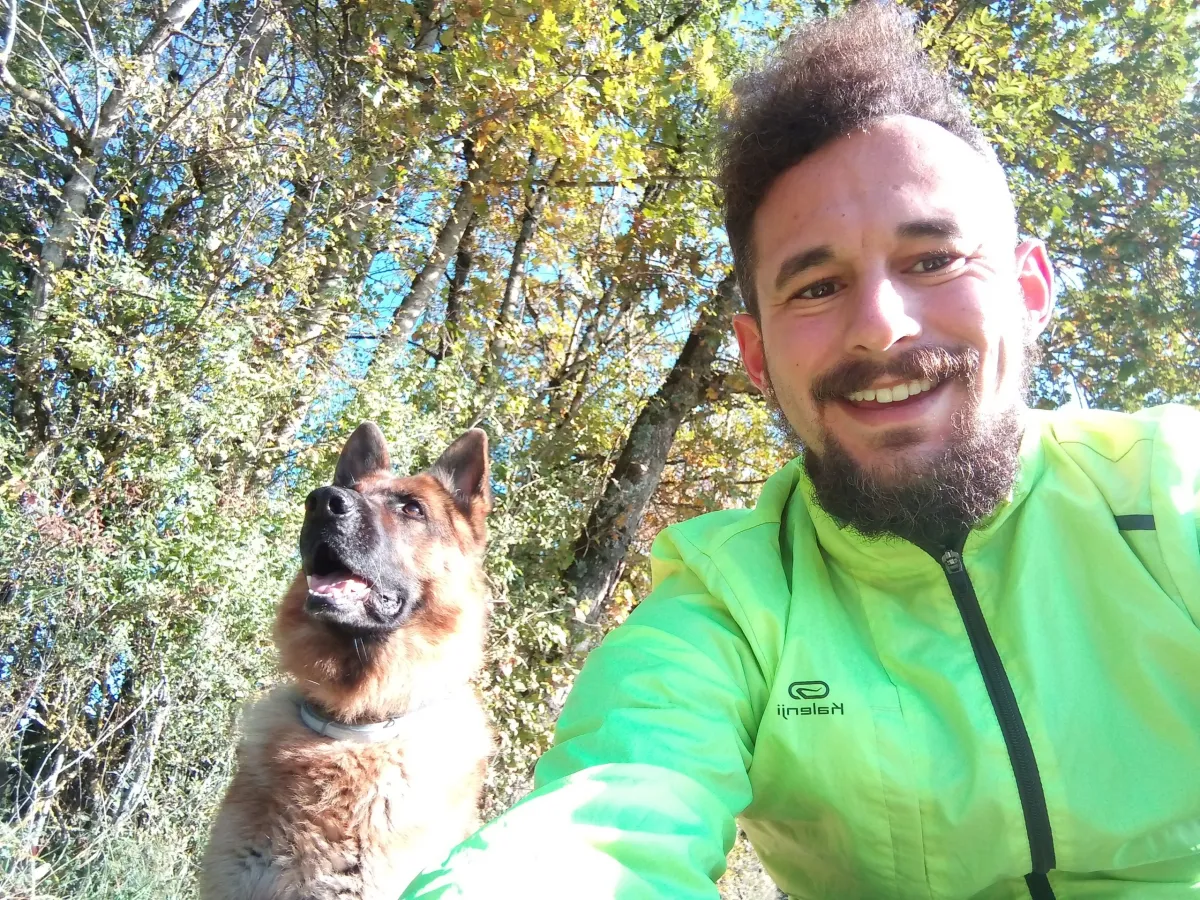 Un pet-sitter en forêt avec un chien fauve et noir